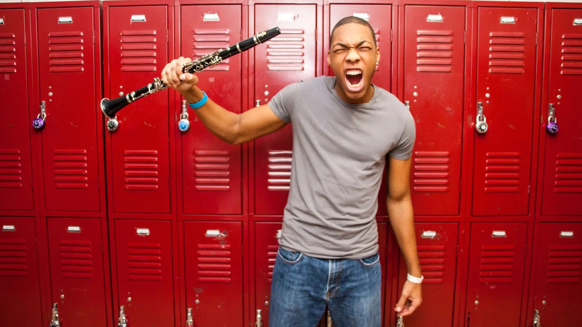 Young person yelling while holding up a clarinet in front of a row of red school lockers