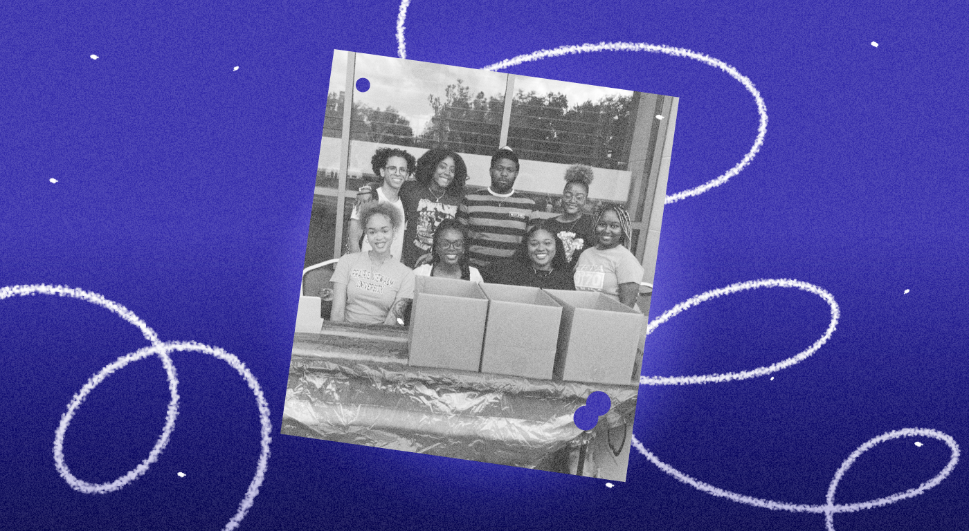 A black and white snapshot of eight young people of color at a table with cardboard boxes