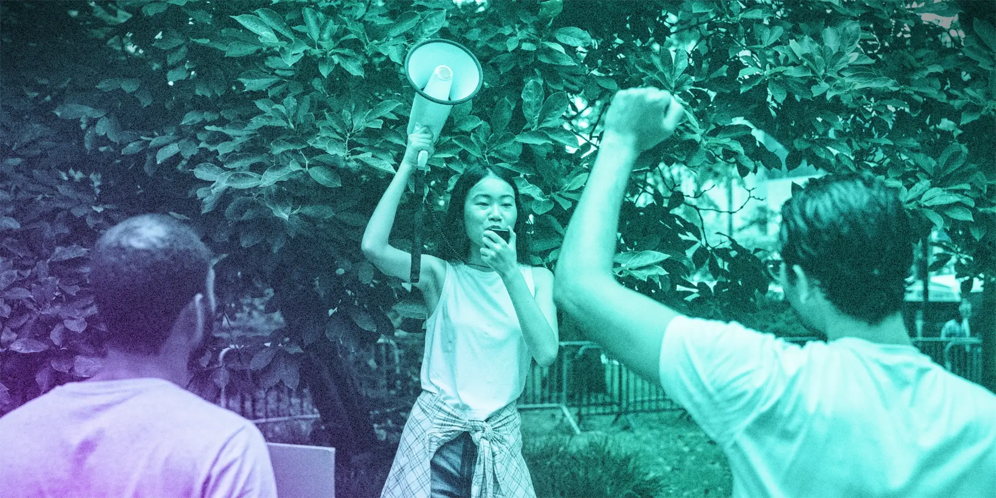 Young person holding up a megaphone in front of 2 people protesting.