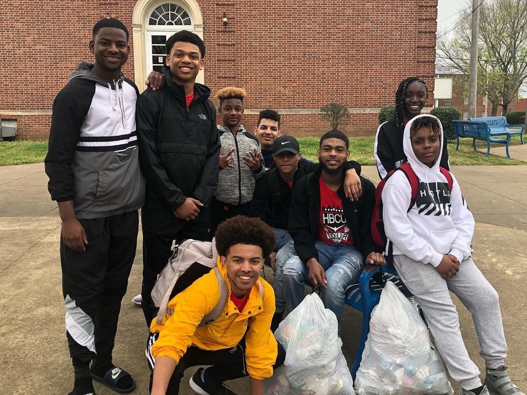 A diverse group of young volunteers poses outdoors after participating in a community clean-up event, holding bags filled with collected litter. The scene highlights teamwork and civic responsibility, showcasing the importance of community service and leadership initiatives.