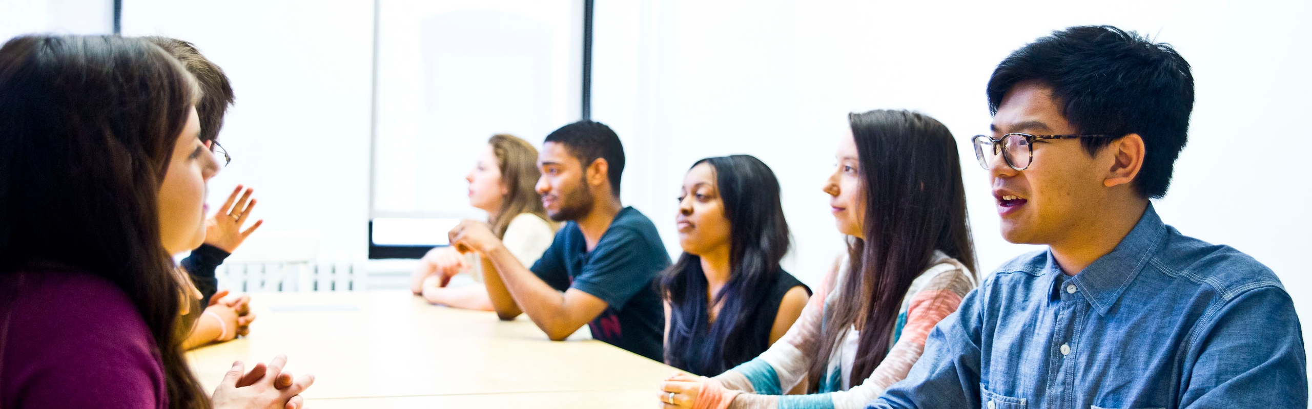 A group of young people speaking to one another across a long conference table