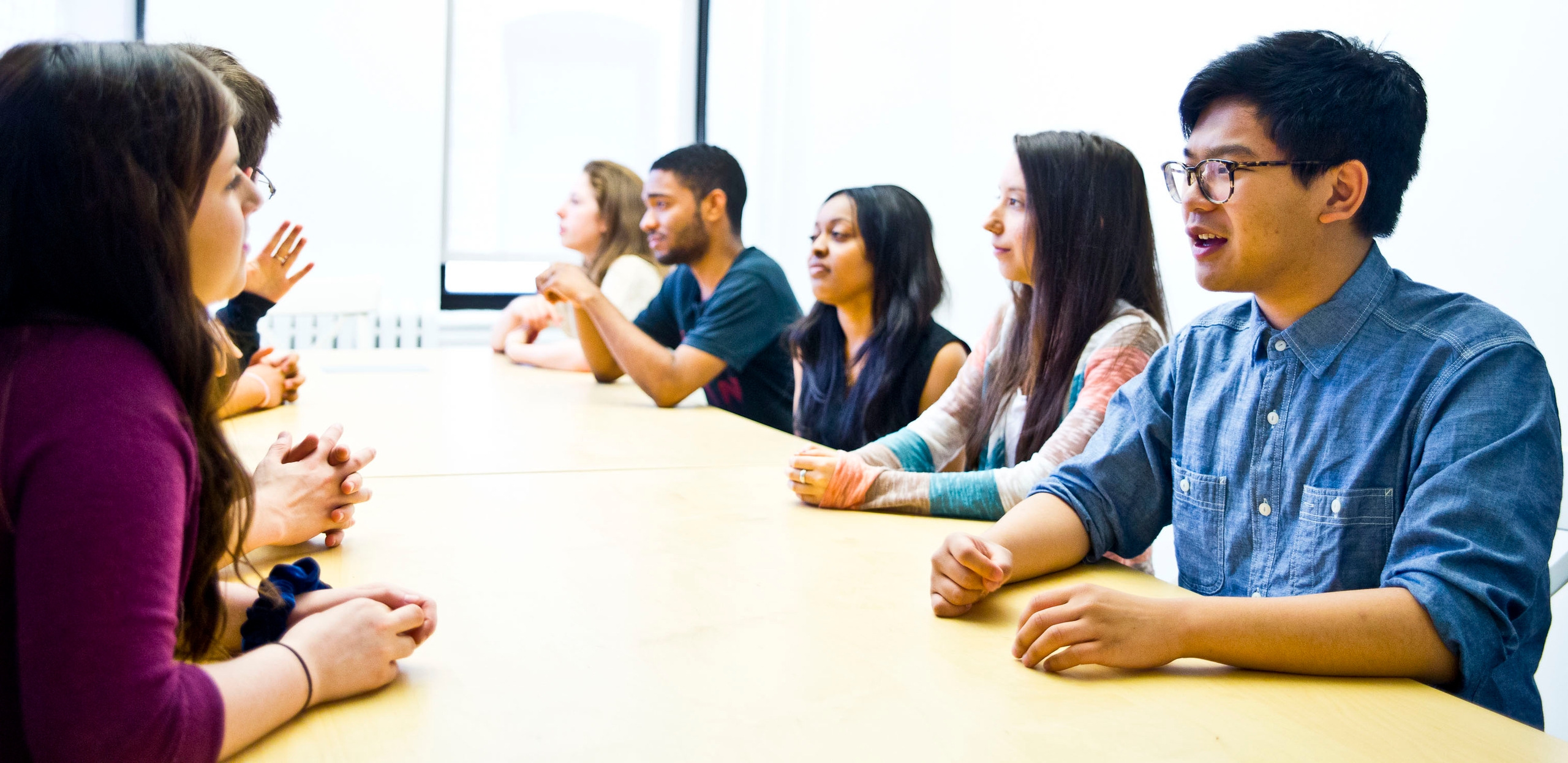 A group of young people speaking to one another across a long conference table