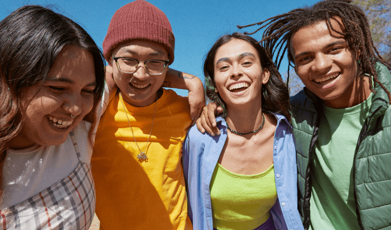 A diverse group of 4 young people in an embrace, smiling joyfully