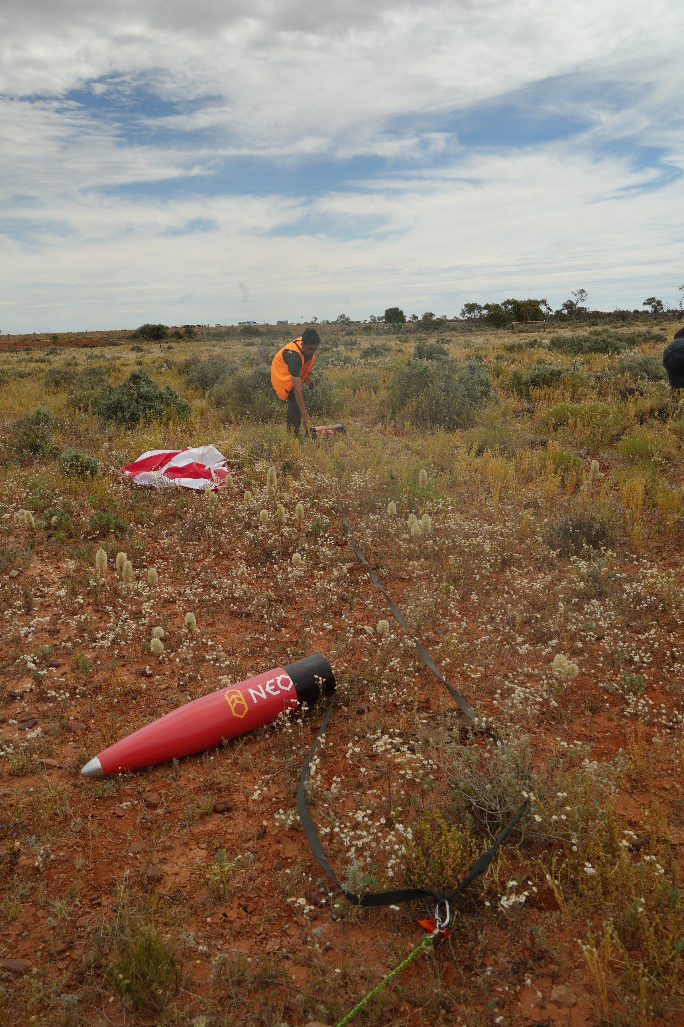 The red nose section of Kronos lies in green and orange scrub with a parachute visible behind it.