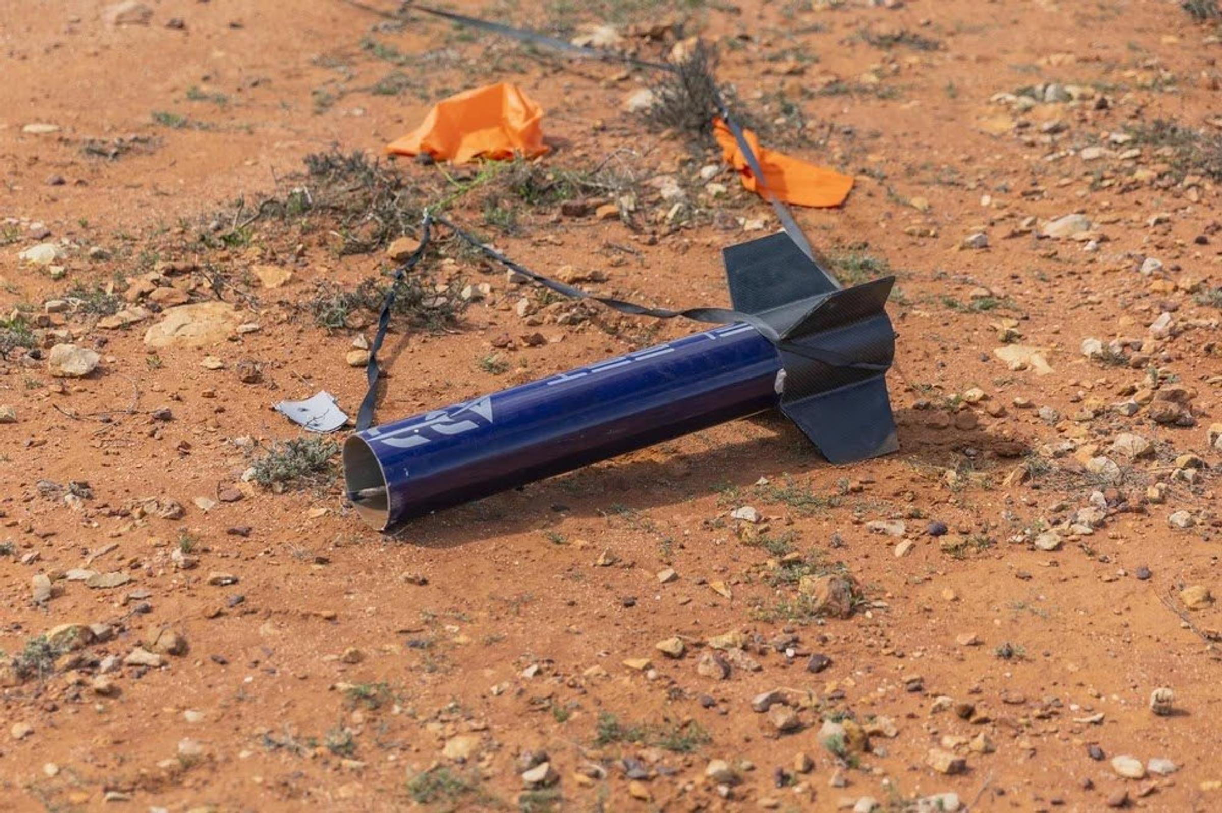 The navy aft section of Myriad with black fins lies on red soil after landing, with orange marker flags nearby.
