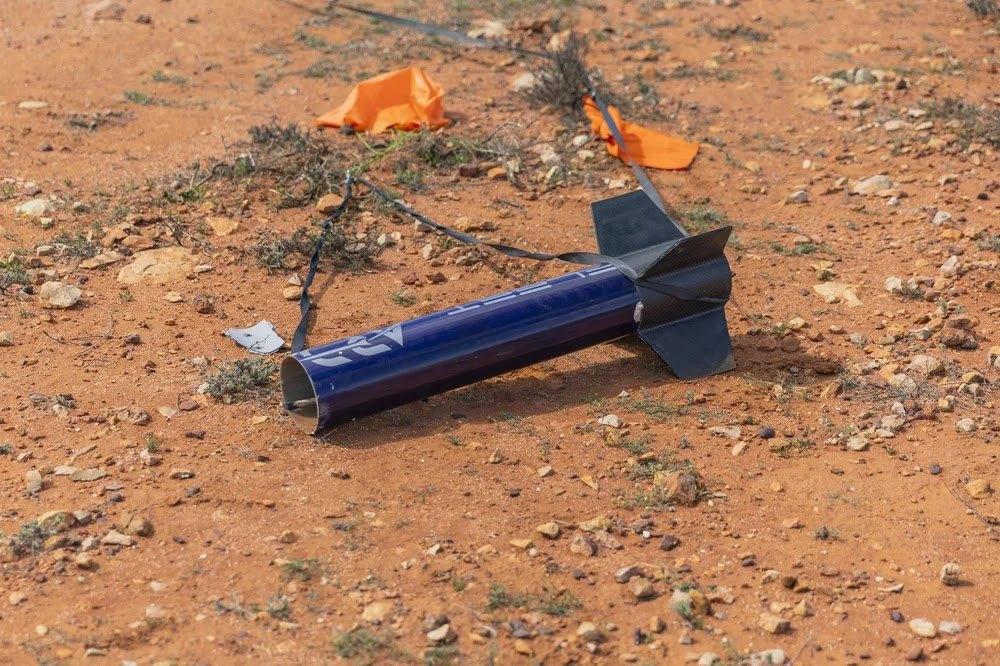 The navy aft section of Myriad with black fins lies on red soil after landing, with orange marker flags nearby.