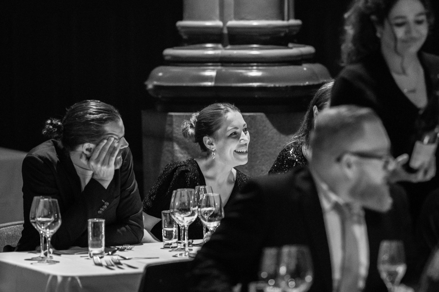 Two colleagues creased up laughing over a formal dinner table.