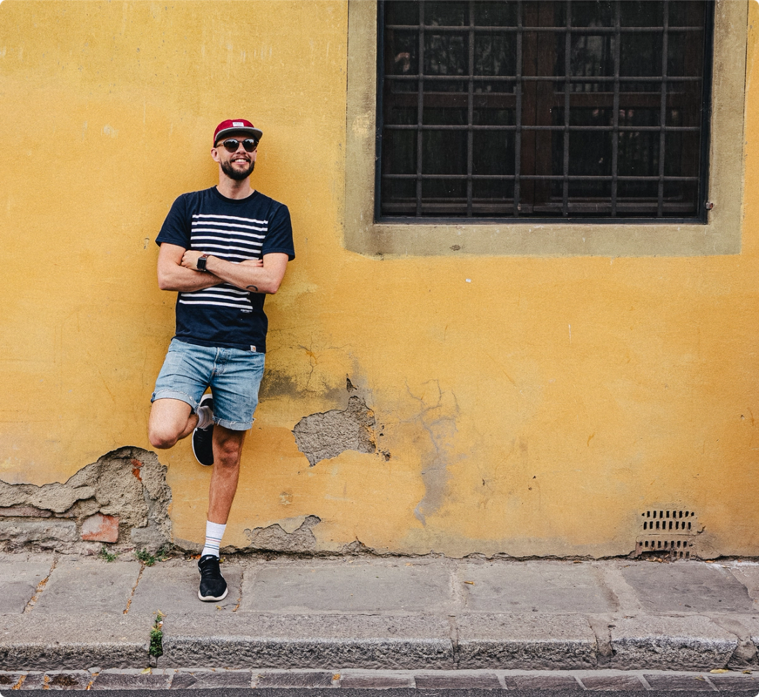 A colleague leaning against a weathered yellow wall in the sun, arms folded.
