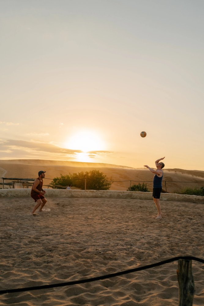 Two colleagues playing beach volleyball as the sun sets behind the dunes.