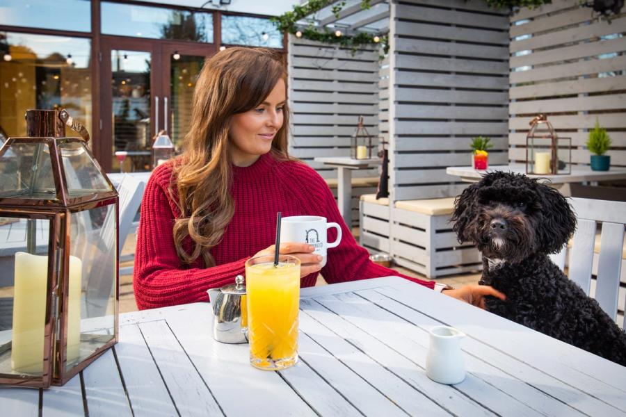 Woman with a coffee and a black dog at a café table outside