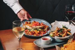 Plates of food and glasses of wine being served at a wooden table