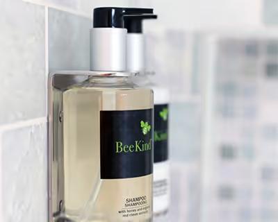 Refillable BeeKind shampoo bottle on a bathroom wall