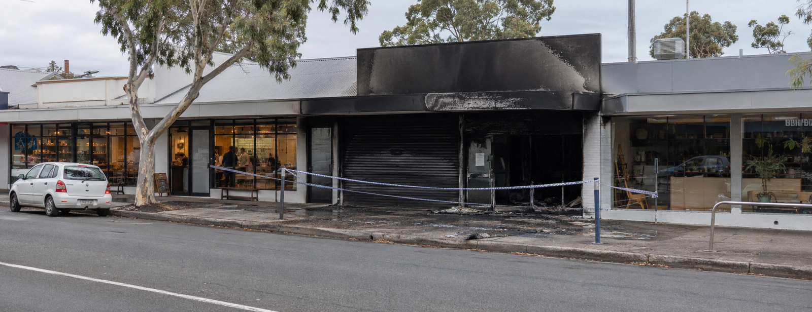 Blackened shopfront cordoned off with tape between neighbouring shops.