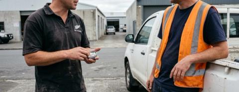 Zwei neuseeländische Arbeiter sprechen neben einem Nutzfahrzeug auf einem Industriegelände über Nikotinbeutel.