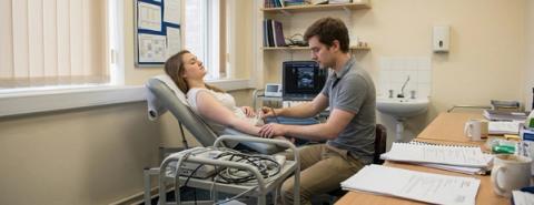 Illustrative image of a clinician using an ultrasound probe on a woman’s arm in a clinic.