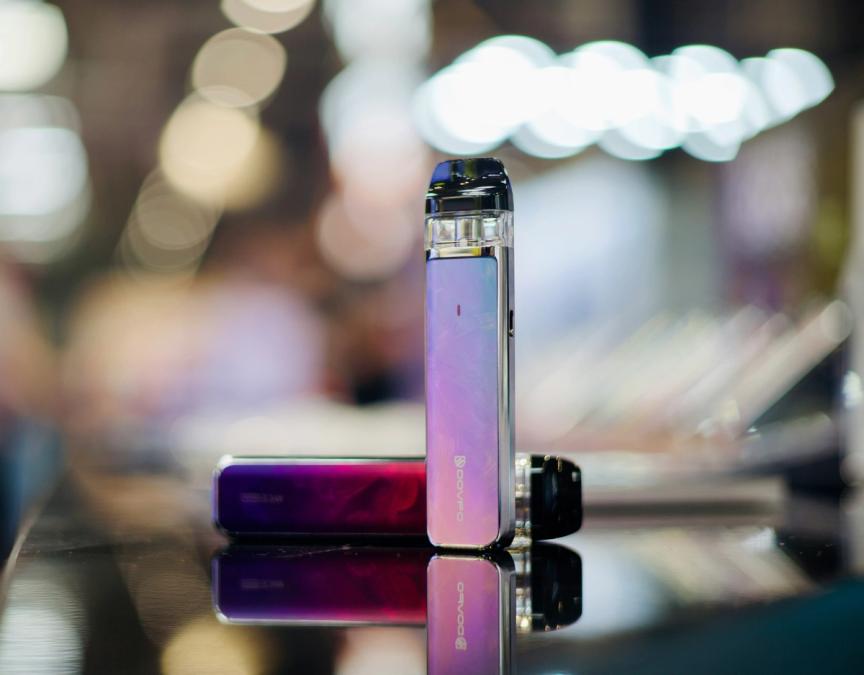 Two purple pod vaping devices on a reflective surface, one upright and one lying horizontally.