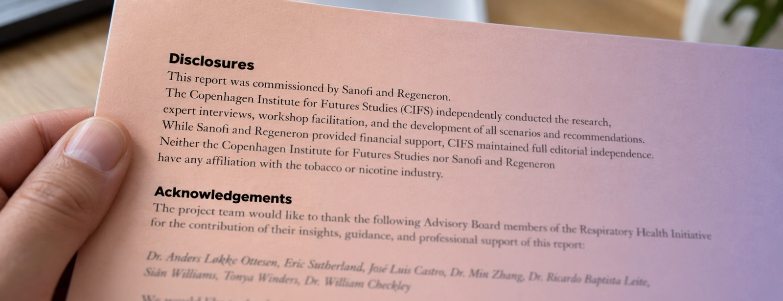 A hand holds a printed disclosure stating that a report was commissioned by Sanofi and Regeneron.