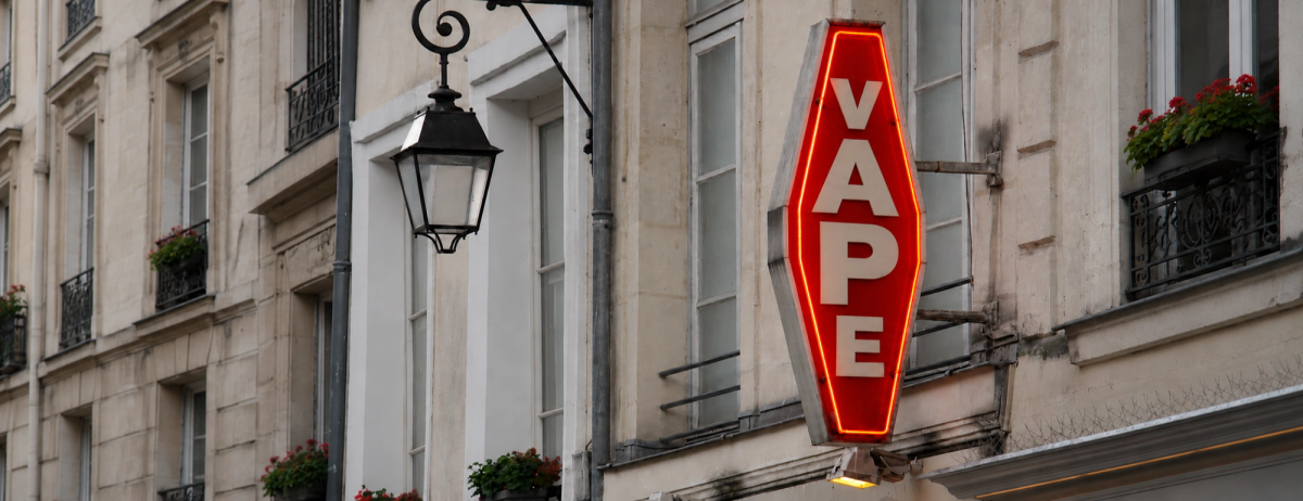 A red illuminated VAPE sign hangs outside a shop on a French street.