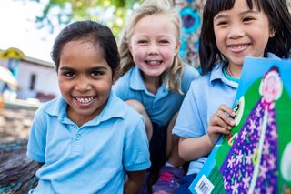 Three kids smiling and holding a book