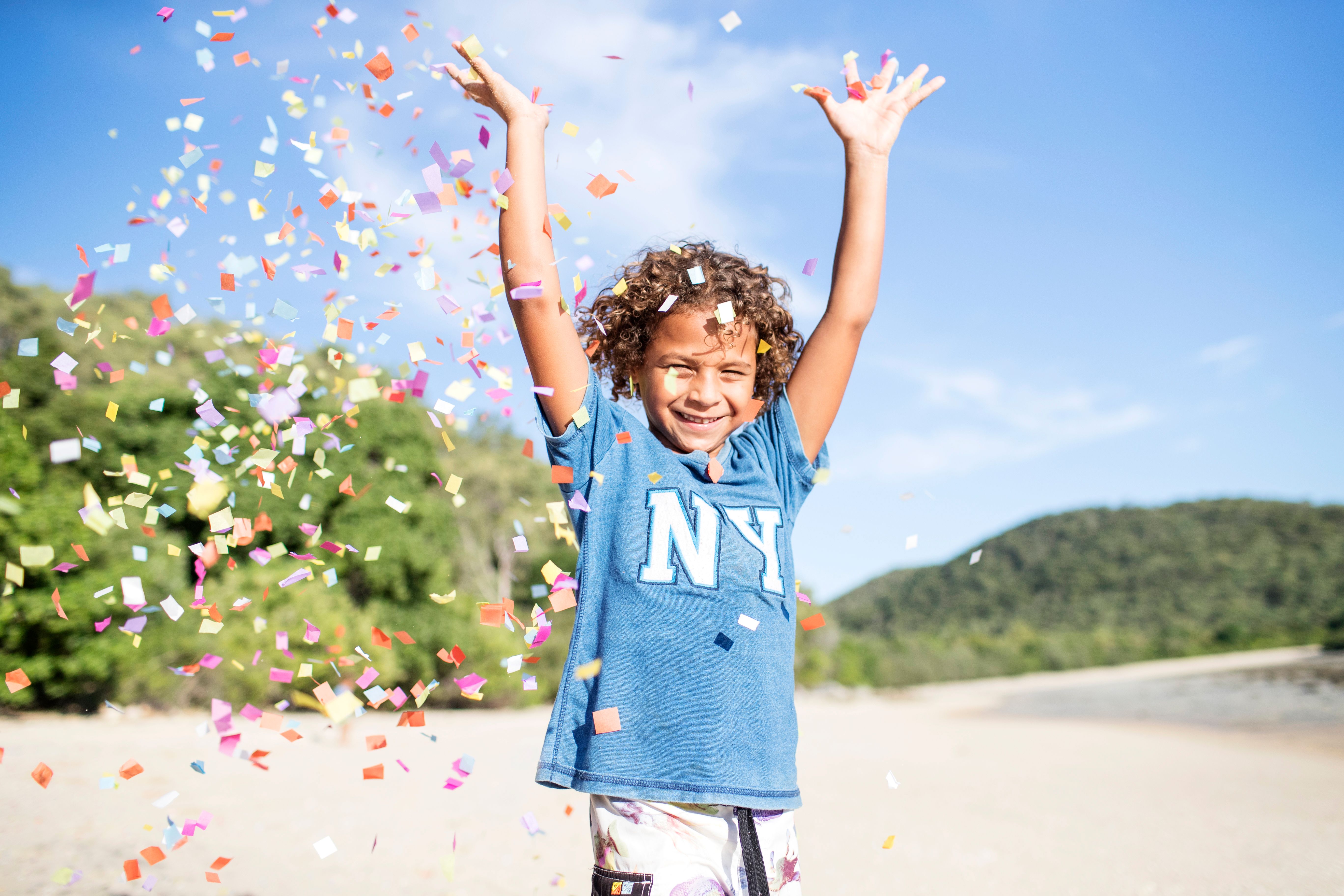 A child on the beach, celebrating with arms in the air and confetti flying around them 