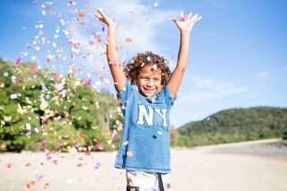 A child on the beach, celebrating with arms in the air and confetti flying around them