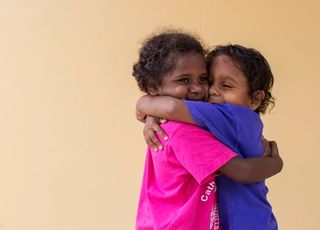 Two kids hugging each other in front of a plain background