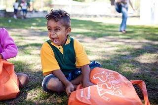 a kid in school uniform, sitting on the grass laughing broadly