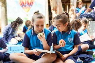 Kids sitting on the ground reading a book and eating apples together
