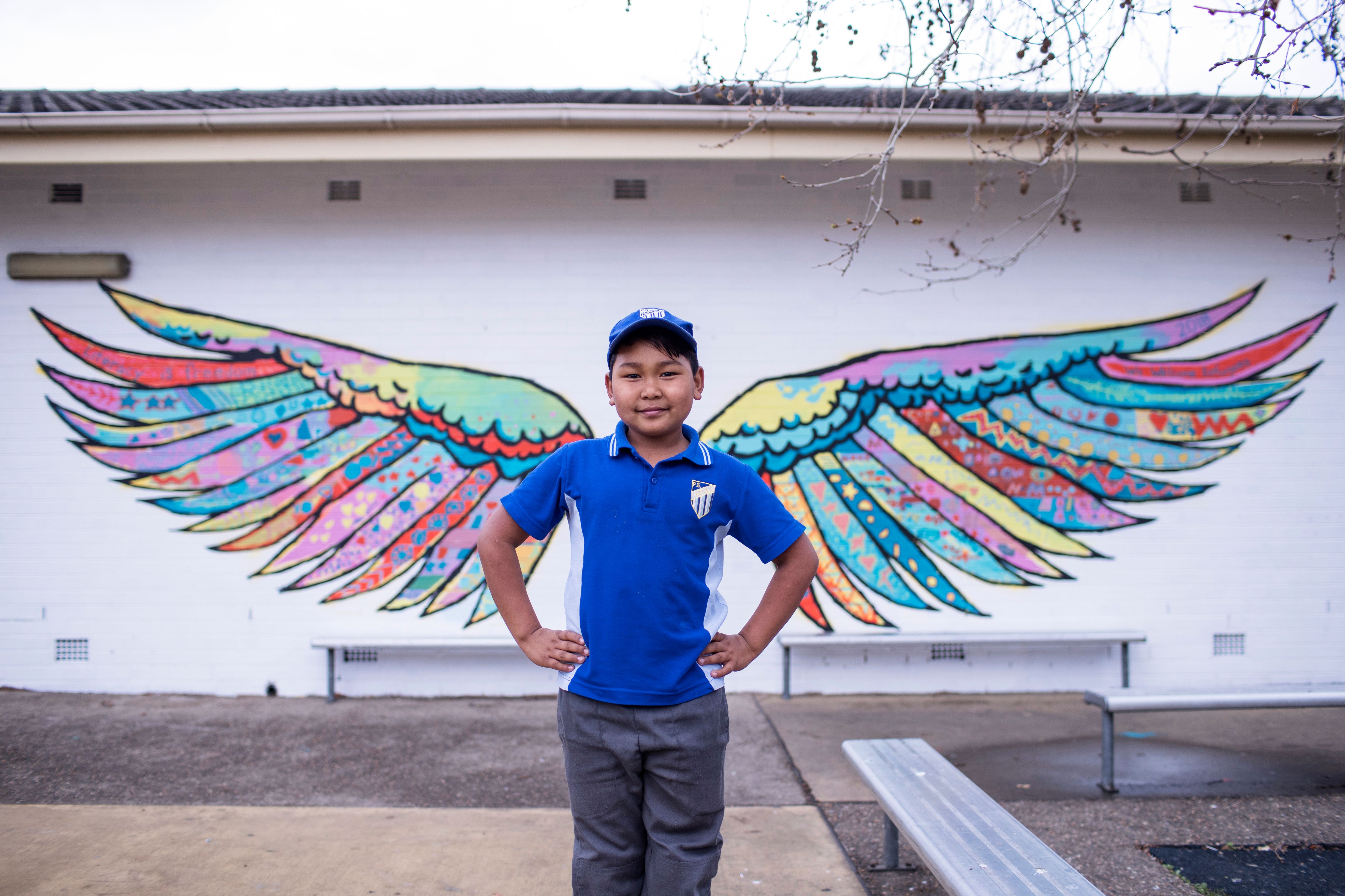 A child facing the camera, with wings graffitied on the wall behind them  