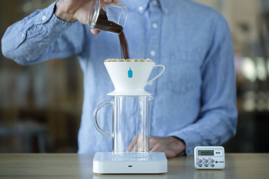 Pouring coffee grinds into a Blue Bottle Coffee pour over dripper