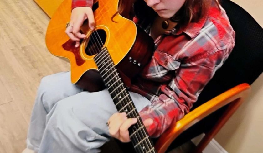 A girl in a plaid shirt playing an acoustic guitar