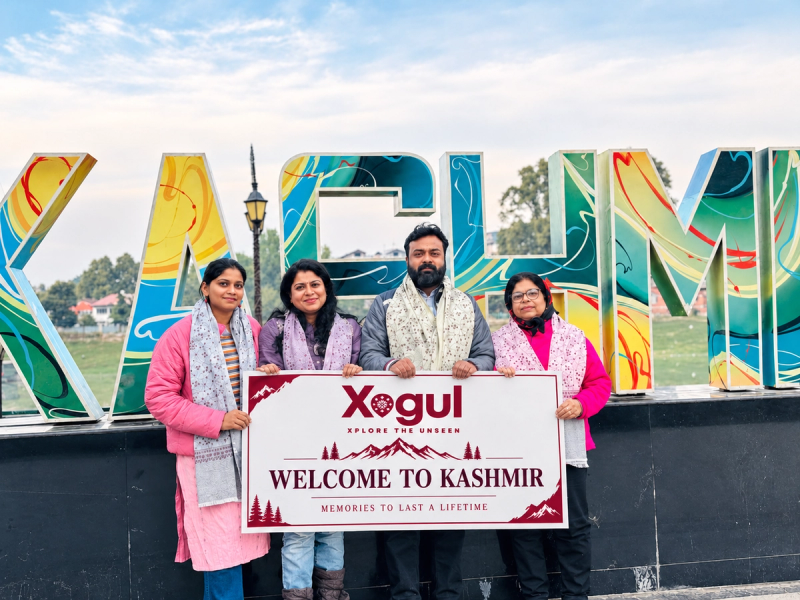 Guests with Kashmiri shawls holding a Xogul welcome board, among Kashmir tour operators for family trips