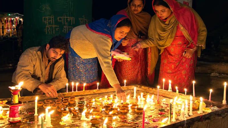 Women in traditional dress lighting diyas and flower petals during Diwali in Kashmir