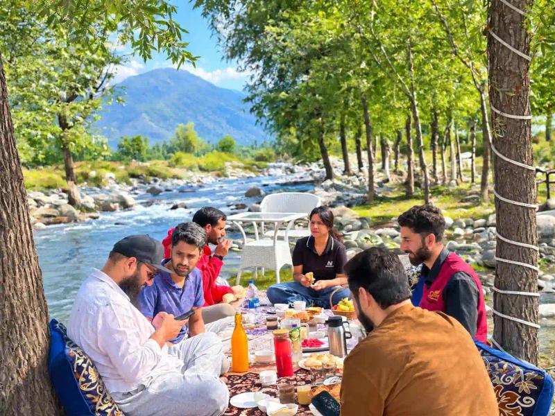 Tourists enjoying a customized riverside picnic and meal in Pahalgam, organized by the best local tour operator in Kashmir for families.