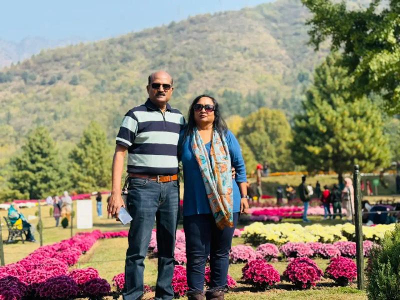 Visitors posing at the Bagh-e-Gul-e-Dawood Srinagar name board with flower beds, a fountain and a gazebo