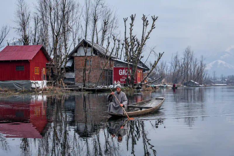 Local boatman rowing a wooden boat on a calm lake, a winter highlight of a Kashmir Tour for Senior Citizens