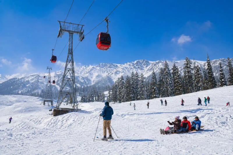 Kashmir 4N/5D Tour Package featuring the Gulmarg Gondola, skiing and sledding activities amid snow-covered mountains.