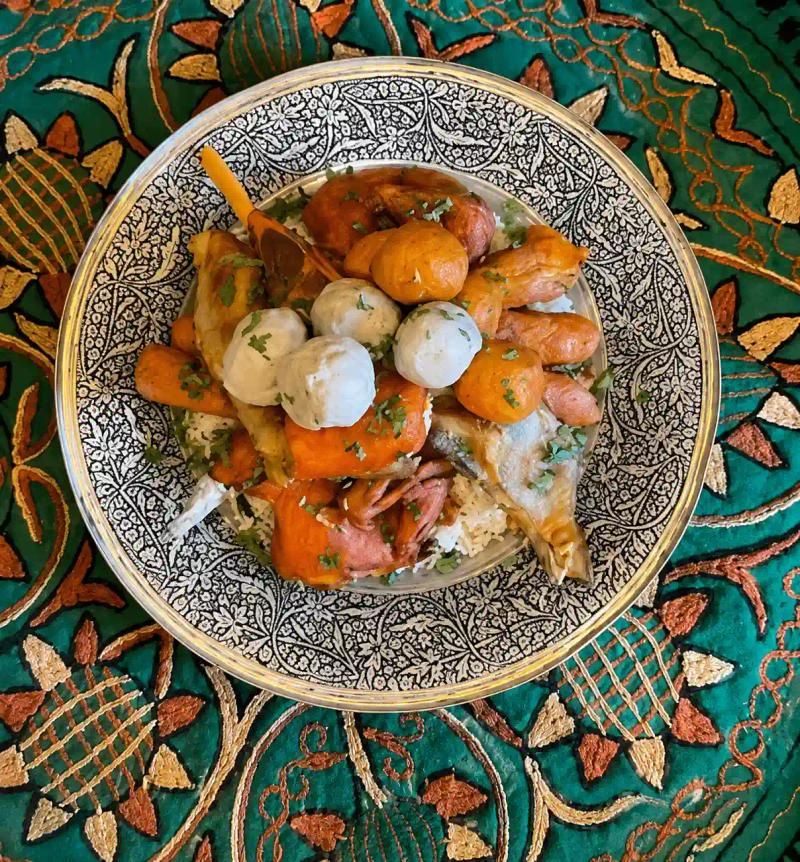 Traditional Wazwan platter served on an ornate Kashmiri plate with rice, chicken, meatballs, and vegetables on a richly embroidered green tablecloth