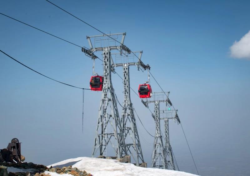Is Kashmir Safe to Visit Right Now – red Gulmarg Gondola cable cars operating above snow-covered mountain slopes under a clear blue sky.