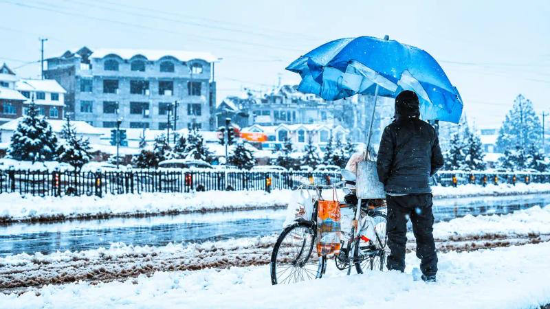 Kashmir winter food and culture during a snowy winter day, showing a local vendor with a bicycle under a blue umbrella.