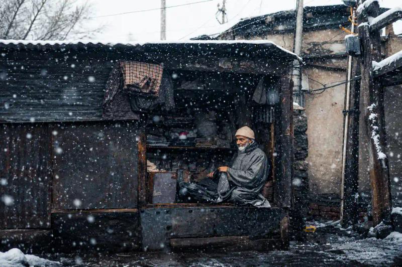 Elderly Kashmiri shopkeeper sitting in his stall during snowfall, local life seen on a Kashmir Tour for Senior Citizens