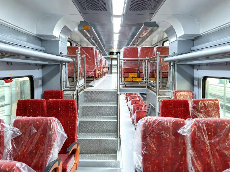 Red-seated train coach interior with steps to an upper level, a look inside a winter train like Vande Bharat Srinagar in winter