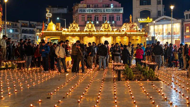 Rows of diyas on a lit city square with a clock tower at night, Diwali in Kashmir