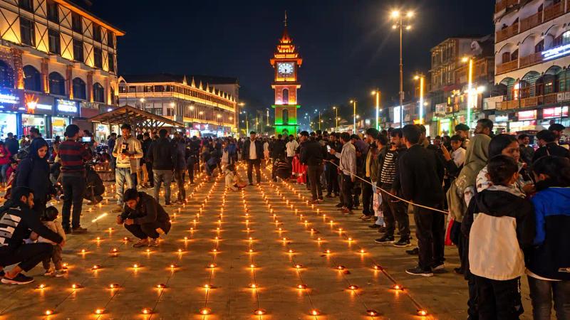 Two people arranging circles of clay lamps in front of a lit temple chariot, Diwali in Kashmir
