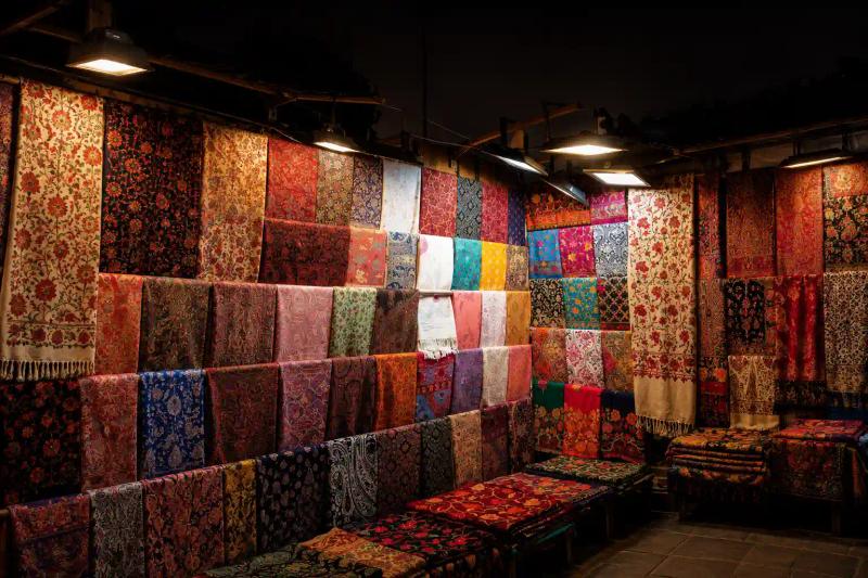 What to Buy in Kashmir – colorful Kashmiri shawls, carpets, and embroidered textiles displayed at a traditional market stall