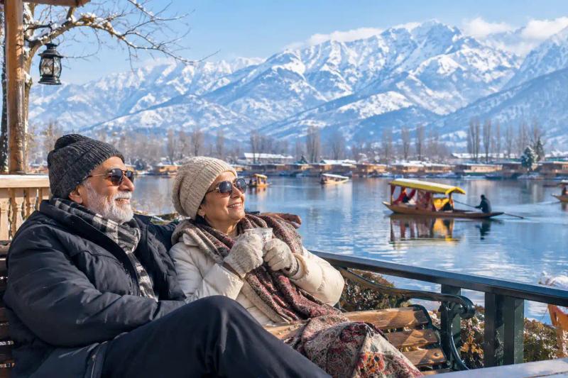 Senior couple enjoying tea on a Kashmir Tour for Senior Citizens with snow-capped mountains and shikaras on the lake