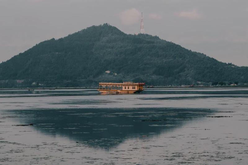 Houseboat on calm water before a forested hill, Dal Lake vs Nigeen Lake in Srinagar