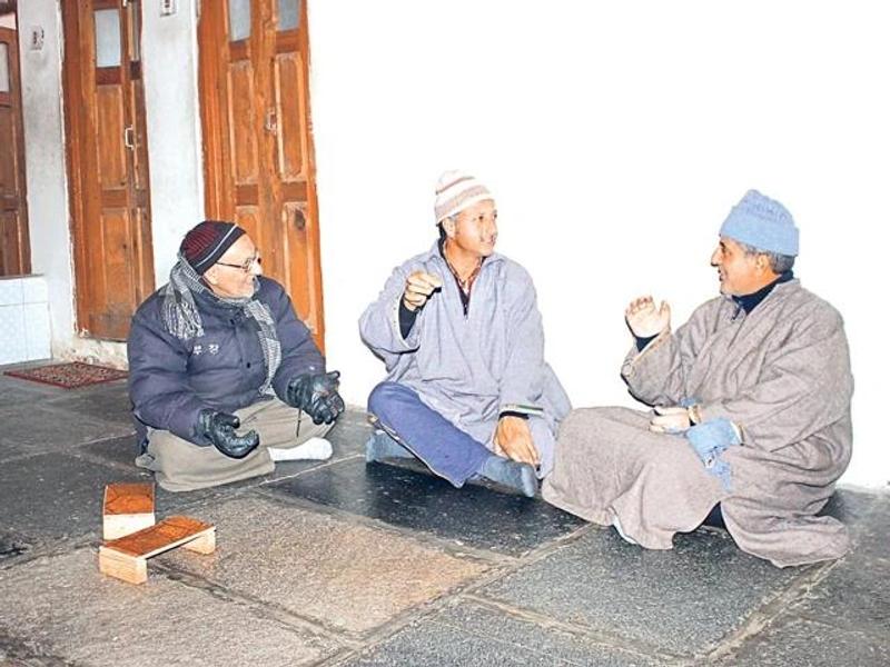Kashmir winter food and culture: three local men in pherans and woollen caps sitting and talking