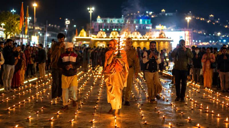Priest carrying a lit aarti lamp through rows of diyas during Diwali in Kashmir