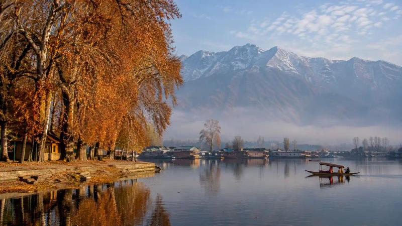 Kashmir in November featuring golden Chinar trees, a shikara on Dal Lake and snow-dusted Himalayan mountains.